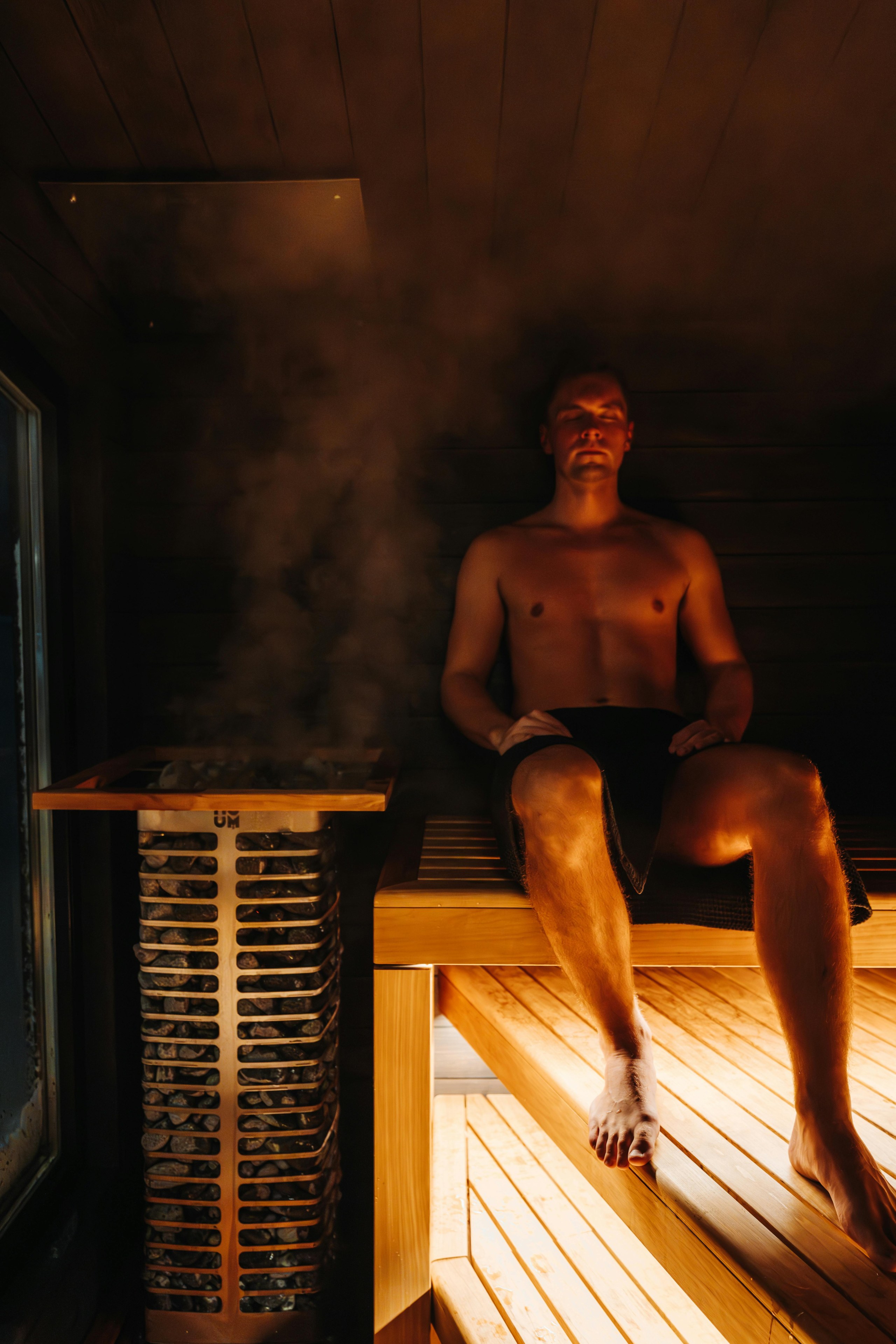 Mies istuu saunassa höyryävän kiukaan vieressä